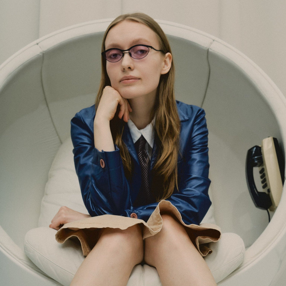 Model in a white pod chair wearing Vincent Catani Alma purple cat-eye sunglasses